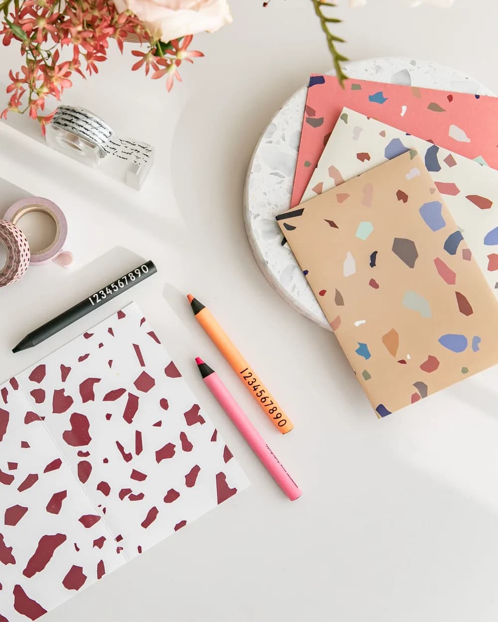 Printed cards in a terrazzo pattern laid out on a desk with pens and washi tape