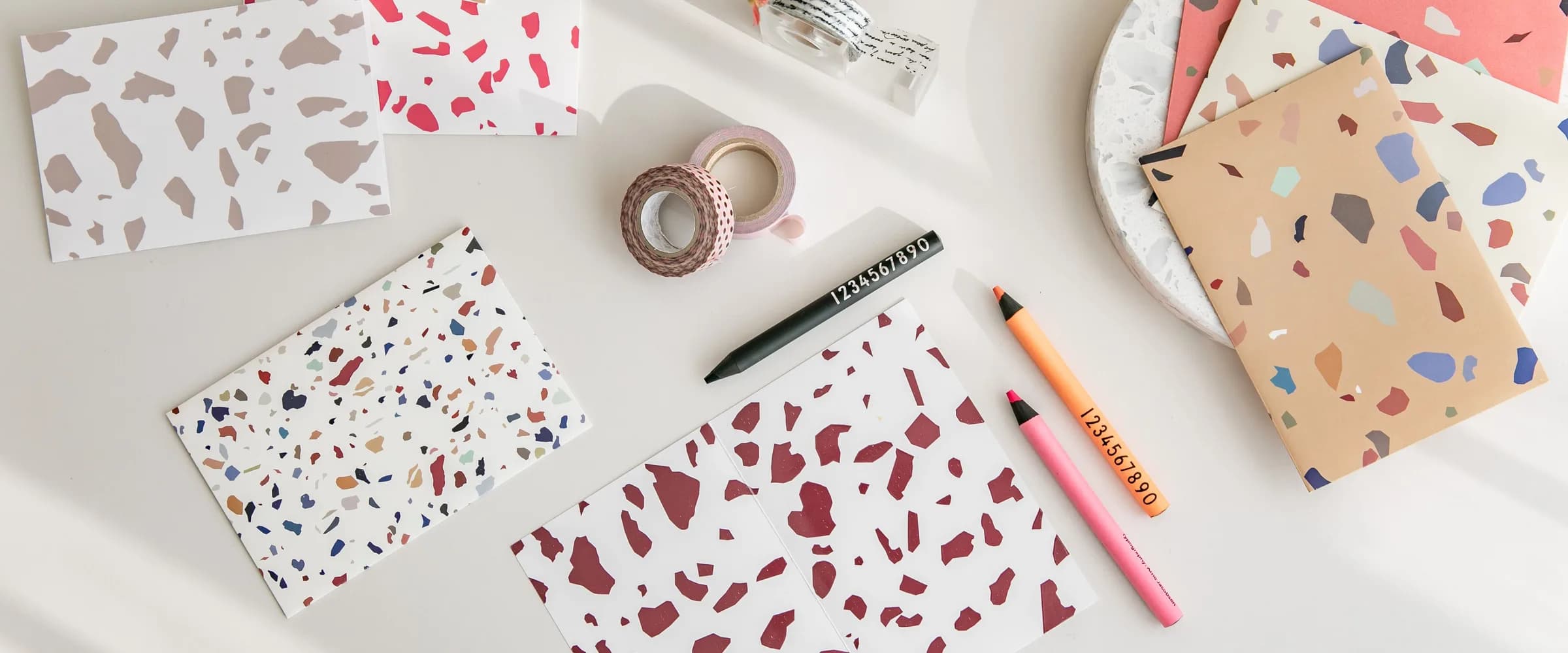 Printed cards in a terrazzo pattern laid out on a desk with pens and washi tape